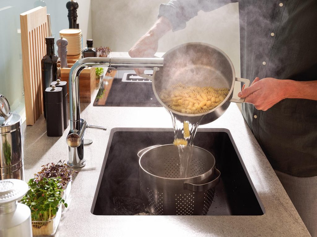 A pot of pasta being drained into a colander in deep Franke Maris granite sink