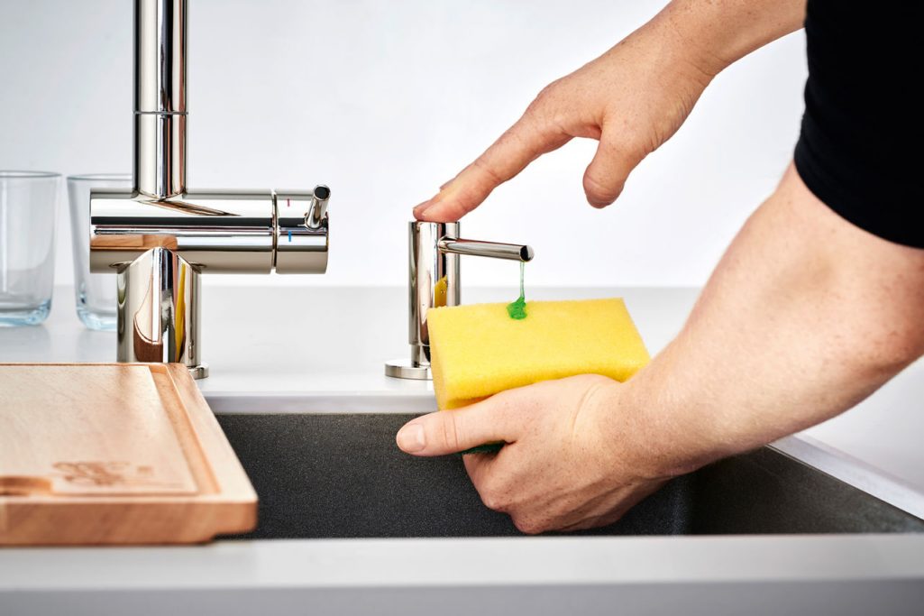 Kitchen sink soap dispenser dipensing soap onto a sponge