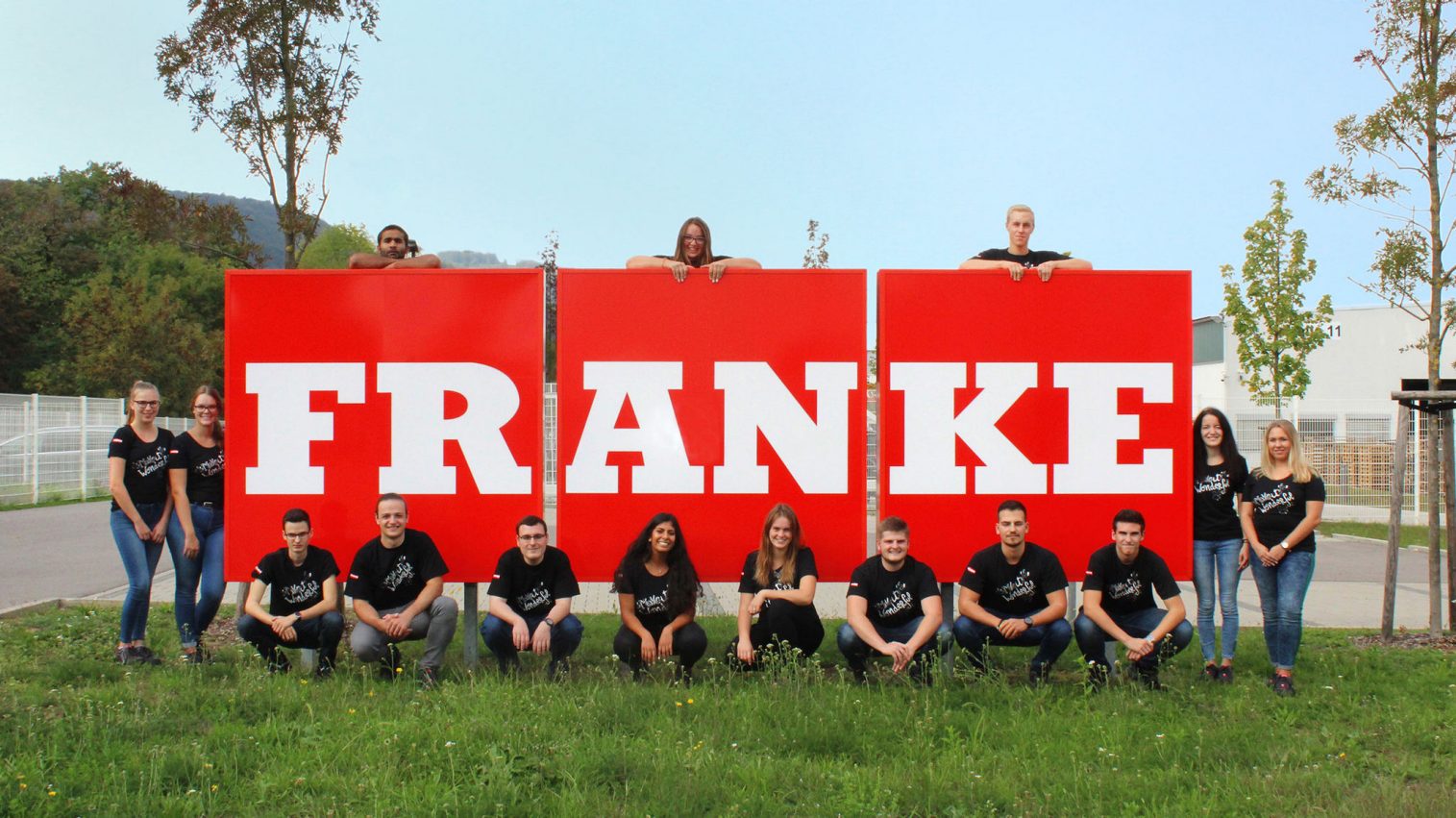 group of young people standing outside in front of the Franke logo